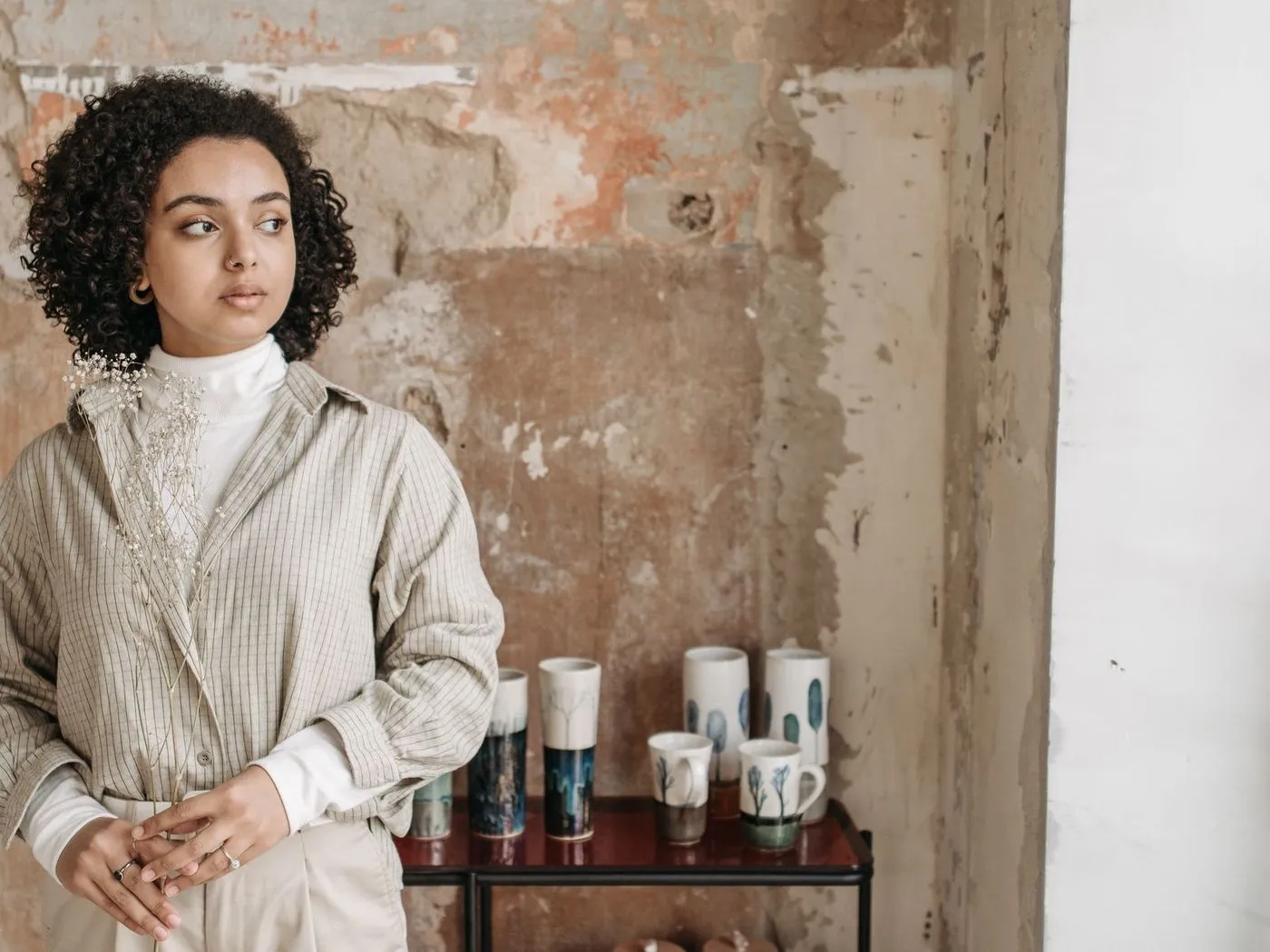 Ceramics maker standing beside a shelf of her handmade mugs and vases